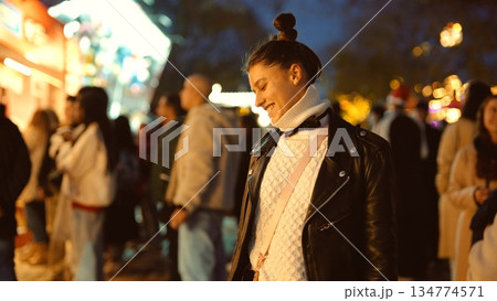 Female individual engaged with mobile amidst bustling market ambiance Female individual engaged with mobile amidst bustling market ambiance 134774571