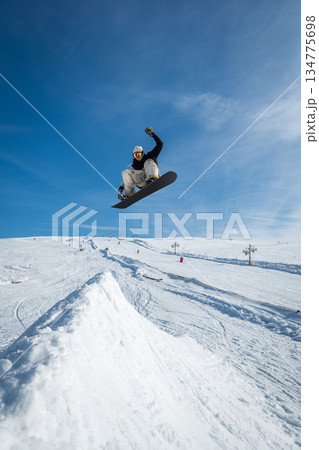 Snowboarder jumping against blue sky Snowboarder jumping against blue sky 134775698