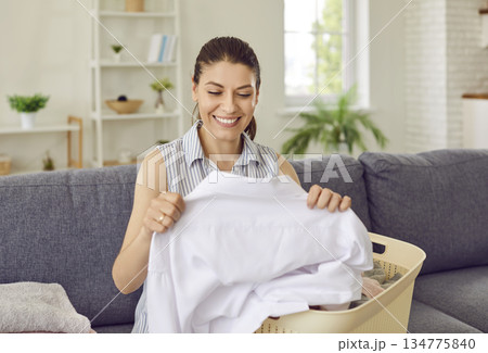 Happy young housewife checking her laundry, looking at clean, white shirt and smiling 134775840