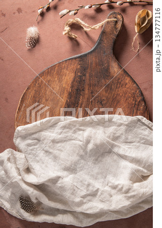Cutting board on a kitchen table with Easter decoration, willow branches, paper eggs and easter festive decorations. Top view, easter holiday mockup concept composition. Cutting board on a kitchen table with Easter decoration, willow branches, paper eggs and easter festive decorations. Top view, easter holiday mockup concept composition. 134777116