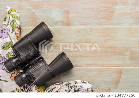 Travel, summer vacation, tourism and objects concept - close up binoculars and scarf on wooden table. Top view with copy space. Travel, summer vacation, tourism and objects concept - close up binoculars and scarf on wooden table. Top view with copy space. 134777250