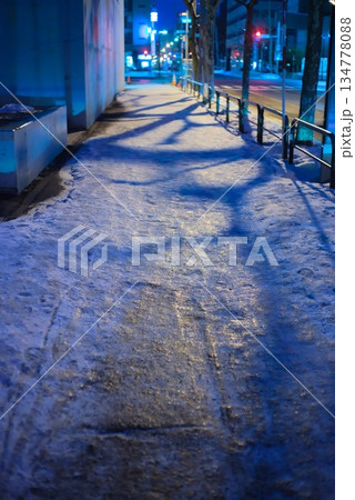 街灯の光が反射し路面凍結や積雪が見られる夜の都市の歩道 街灯の光が反射し路面凍結や積雪が見られる夜の都市の歩道 134778088