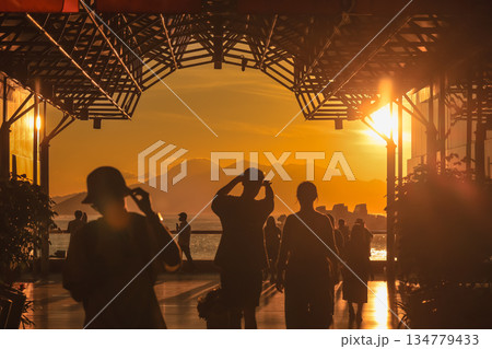 Oct 1 2025 Silhouetted Visitors at Sunset Pier Overlooking Ocean With Mountain 134779433