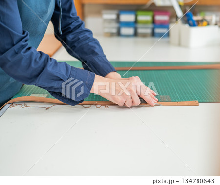Leatherworker measuring and cutting leather in workshop.  134780643