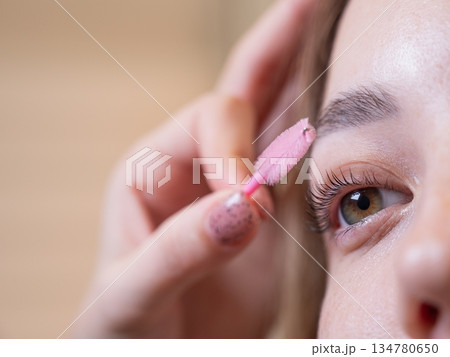 Caucasian woman brushing her eyelashes after lamination. Caucasian woman brushing her eyelashes after lamination. 134780650