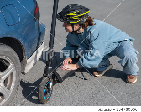 A distressed woman examines the damage after a collision between an electric scooter and a car. 134780666