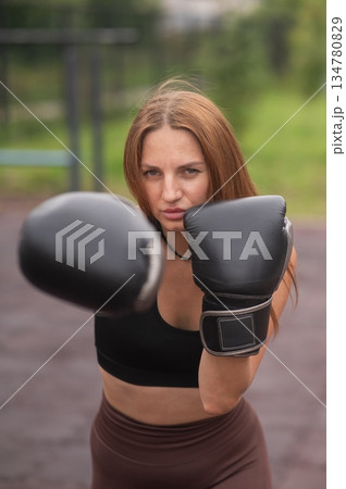 A Caucasian woman practices boxing outdoors.  134780829