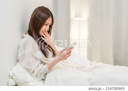 夜ベッドに入りスマホを見る若いアジア人女性 夜ベッドに入りスマホを見る若いアジア人女性 134780903