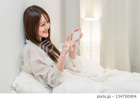 夜ベッドに入りスマホを見る若いアジア人女性 夜ベッドに入りスマホを見る若いアジア人女性 134780904