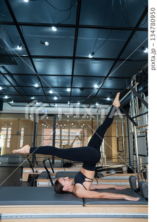 Caucasian woman doing leg exercise on reformer machine. Caucasian woman doing leg exercise on reformer machine. 134780950