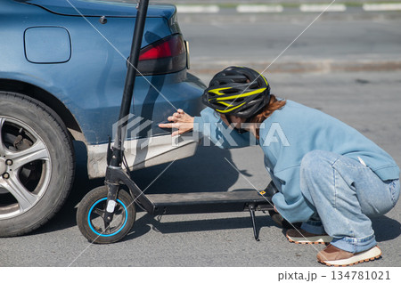 A distressed woman examines the damage after a collision between an electric scooter and a car. A distressed woman examines the damage after a collision between an electric scooter and a car. 134781021