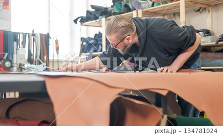 Caucasian bearded man working as a tanner in a workshop.  134781024