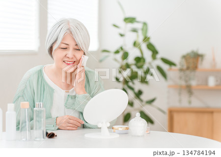 肌を保湿するためにスキンケアするグレイヘアーのシニア女性 肌を保湿するためにスキンケアするグレイヘアーのシニア女性 134784194