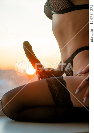 A woman holds a black vibrator near her panties.  134784373