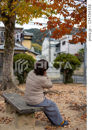 秋の公園で一人ベンチに座る中高年女性 秋の公園で一人ベンチに座る中高年女性 134784388