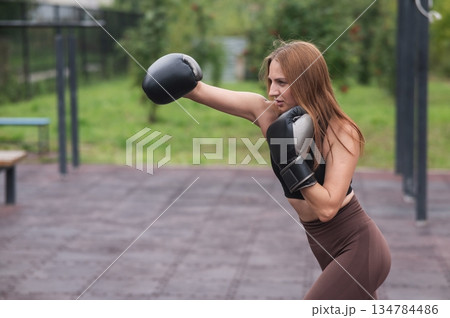 A Caucasian woman practices boxing outdoors.  134784486