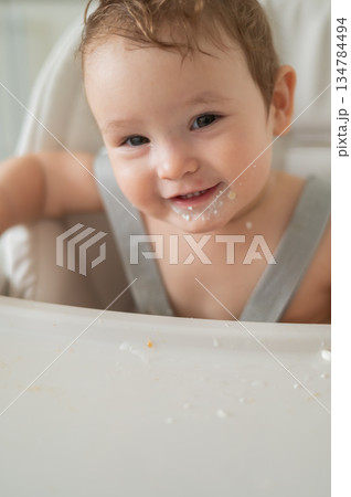Cute baby boy smeared in sour cream sits in a high chair. Cute baby boy smeared in sour cream sits in a high chair. 134784494