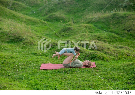 Caucasian woman doing yoga with her little son outdoors.  134784537