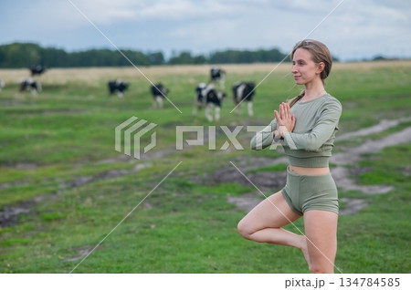 Caucasian woman doing yoga in rural area among herd of cows. Caucasian woman doing yoga in rural area among herd of cows. 134784585
