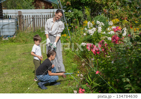 Caucasian woman tending her garden with her sons. Caucasian woman tending her garden with her sons. 134784630