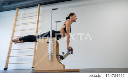 Caucasian woman doing Pilates on classic chair. Caucasian woman doing Pilates on classic chair. 134784662