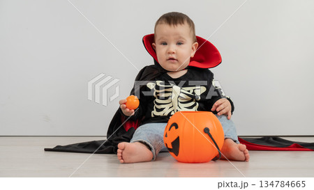 Cute caucasian boy in dracula halloween costume holding candy basket on white background.  134784665