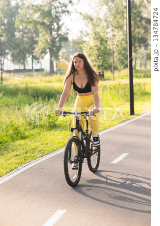 Curvy Caucasian Woman Riding Bicycle in Park.  134784724