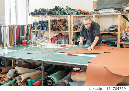 Caucasian bearded man working as a tanner in a workshop.  134784759