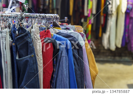 Colorful variety of vintage apparel and second-hand clothes hanging on a rack in a thrift shop or flea market. This image captures the concept of sustainable fashion, retro style, and the treasure 134785887