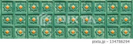 Green carved wooden door panel with orange studs 134786294