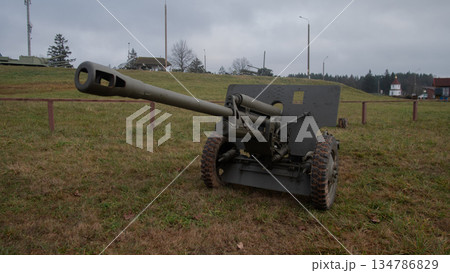 vintage field gun with long barrel on open field under cloudy sky; museum reenactment crew preparing static vintage field gun with long barrel on open field under cloudy sky; museum reenactment crew preparing static 134786829