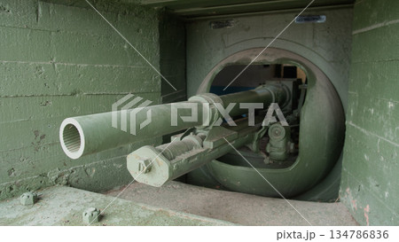 cannon barrel peering through armored turret toward open field, heavy mount and breech visible, olive surfaces 134786836