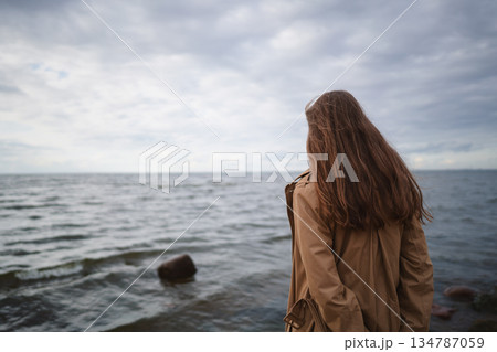 pretty girl walking on a beach in beige trench coat from behind pretty girl walking on a beach in beige trench coat from behind 134787059