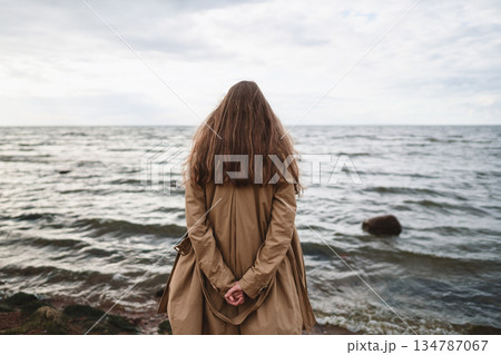 pretty girl walking on a beach in beige trench coat from behind pretty girl walking on a beach in beige trench coat from behind 134787067