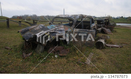 vehicles damaged chaos, scattered wreckage on hillside, disordered cars and twisted metal in chaos scene, scattered wrecked automobiles on grassy knoll with mangled metal and burnt panels 134787073
