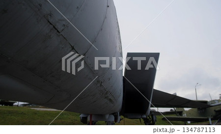 wide underside perspective showing open ventral bay and cargo ramp silhouette, dark interior throat contrasted with gray skin and landing gear struts, cloudy sky and damp ground conveying maintenance 134787113