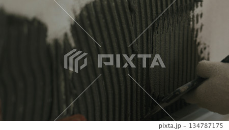 closeup worker applying concrete glue to wall before applying brick tile 134787175
