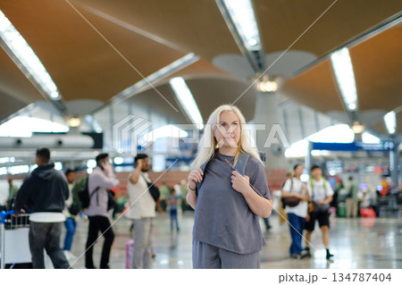 Woman standing in a busy international airport terminal with people walking around and modern architecture in the background during daytime travel hours Woman standing in a busy international airport terminal with people walking around and modern architecture in the background during daytime travel hours 134787404