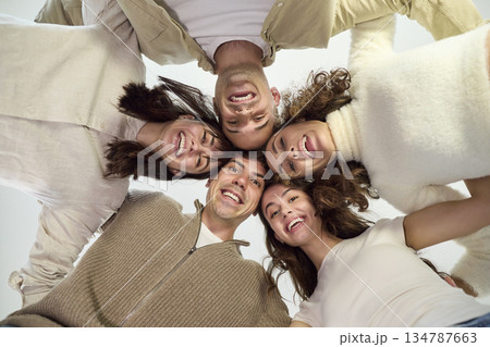 Smiling group of young friends in circle, playful huddle portrait from below Smiling group of young friends in circle, playful huddle portrait from below 134787663
