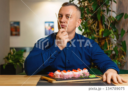 Man sits thoughtfully with chopsticks, contemplating his sushi selection. Man sits thoughtfully with chopsticks, contemplating his sushi selection. 134789075