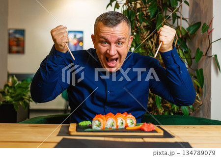 Happy man raises his fists, excited to enjoy a fresh sushi assortment. Happy man raises his fists, excited to enjoy a fresh sushi assortment. 134789079