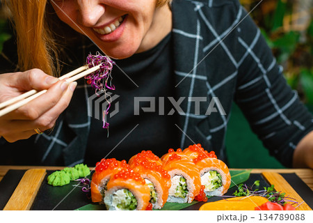 Tight shot of a woman holding chopsticks over a vibrant sushi assortment. Tight shot of a woman holding chopsticks over a vibrant sushi assortment. 134789088