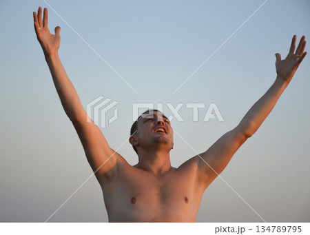 A shirtless man standing with his arms raised 134789795