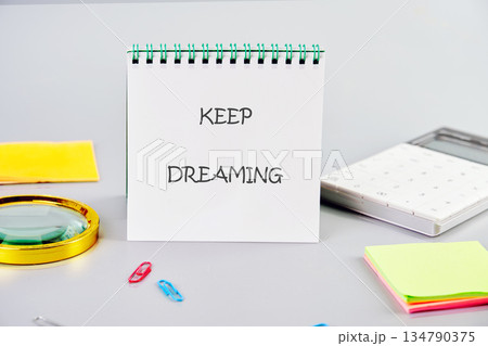 On a light gray table, a notepad displays the message KEEP DREAMING On a light gray table, a notepad displays the message KEEP DREAMING 134790375