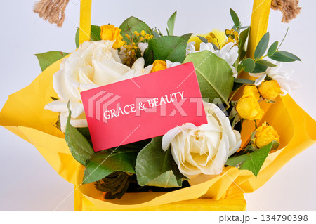 A charming arrangement displays vibrant white roses, miniature yellow roses, and dainty white blossoms, nestled in a yellow wooden box with a card expressing, Grace and Beauty A charming arrangement displays vibrant white roses, miniature yellow roses, and dainty white blossoms, nestled in a yellow wooden box with a card expressing, Grace and Beauty 134790398