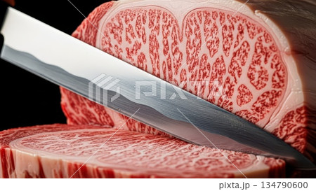 Premium wagyu beef ribeye steak being sliced with sharp knife showing intricate marbling pattern and fat distribution on cutting board 134790600