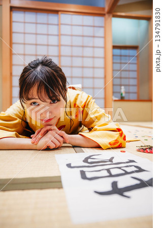 和室で書道の作品を置き横になる若い着物の女性 134791830