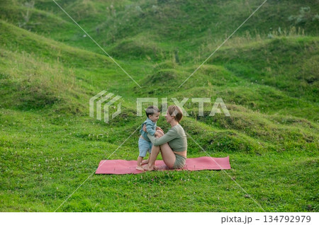 Caucasian woman doing yoga with her little son outdoors.  134792979