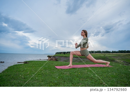 Caucasian woman doing yoga on the river bank. Warrior pose. Caucasian woman doing yoga on the river bank. Warrior pose. 134792980