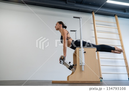 Caucasian woman doing Pilates on classic chair. Caucasian woman doing Pilates on classic chair. 134793108